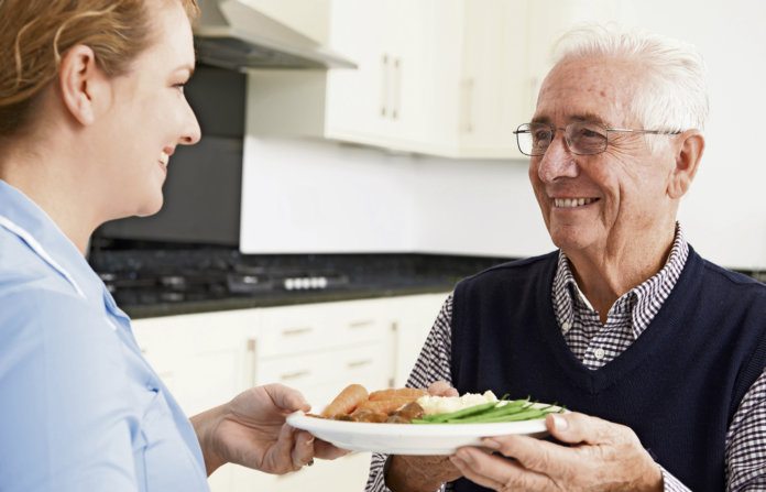 Carer Serving Lunch To Senior Man